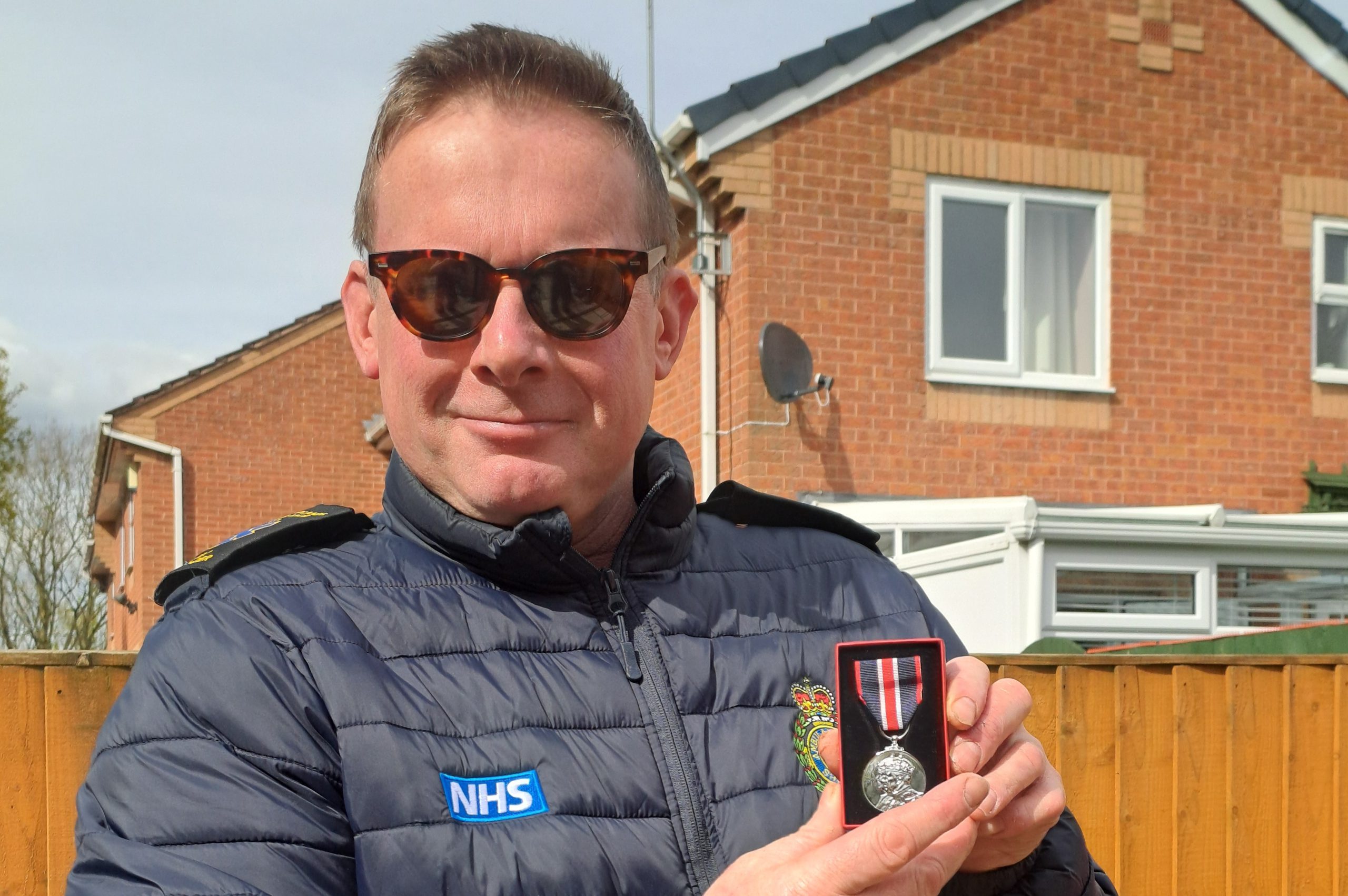 Construction teacher Michael Grange wearing sunglasses and a black gilet, holding his King's Coronation Medal