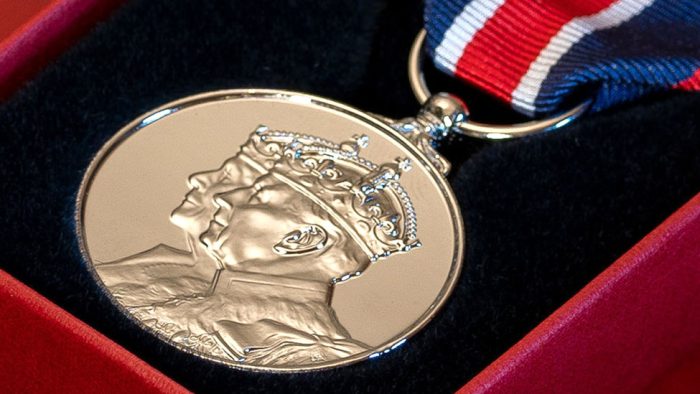 A silver medal with portraits of King Charles and Queen Camilla.