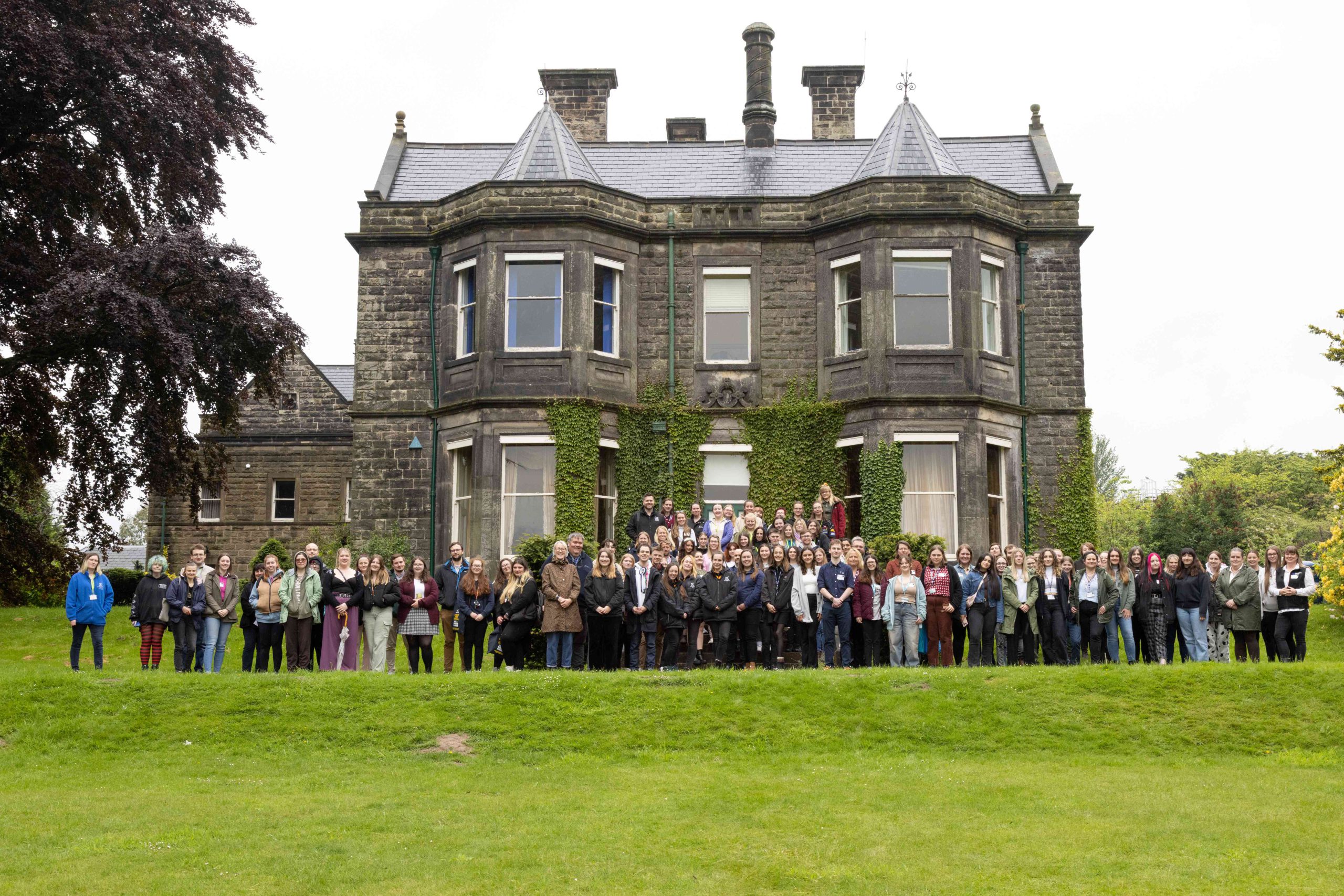 Students and other attendees at the Inter-College Challenge stood on grass infront of an old stone building, the Old Hall at Broomfield Hall