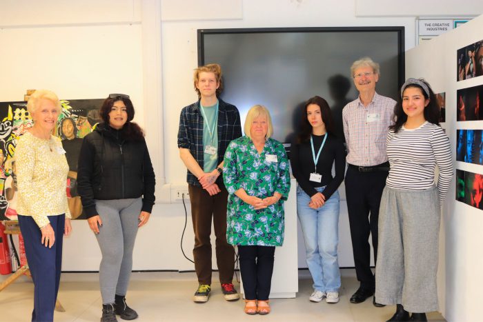 Group of art judges and art & design students stood in front of a screen.