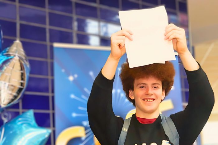 Young man smiling and hoilding his results certificate aloft.