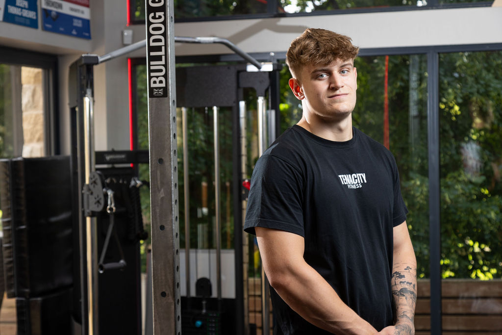 Young man stood by a weights machine.