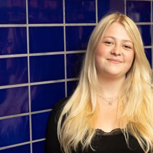 Girl leaning against a blue tiled wall.