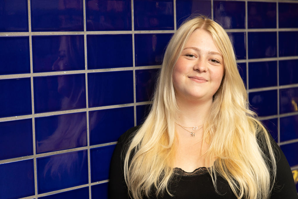 Girl leaning against a blue tiled wall.