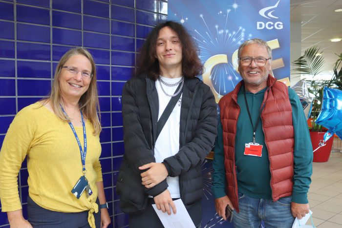 Young man holding a piece of paper, stood with two older people, his father and his teacher.