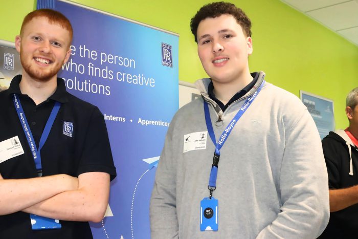 Two smiling men from Rolls Royce group stood in front of a blue banner at Derby College Group's Broomfield Hall.