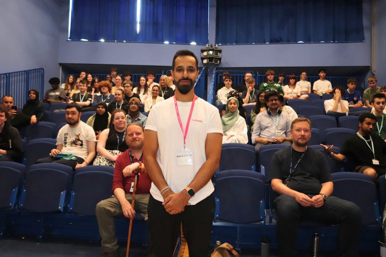 Young male stood in front of an audience of college students.