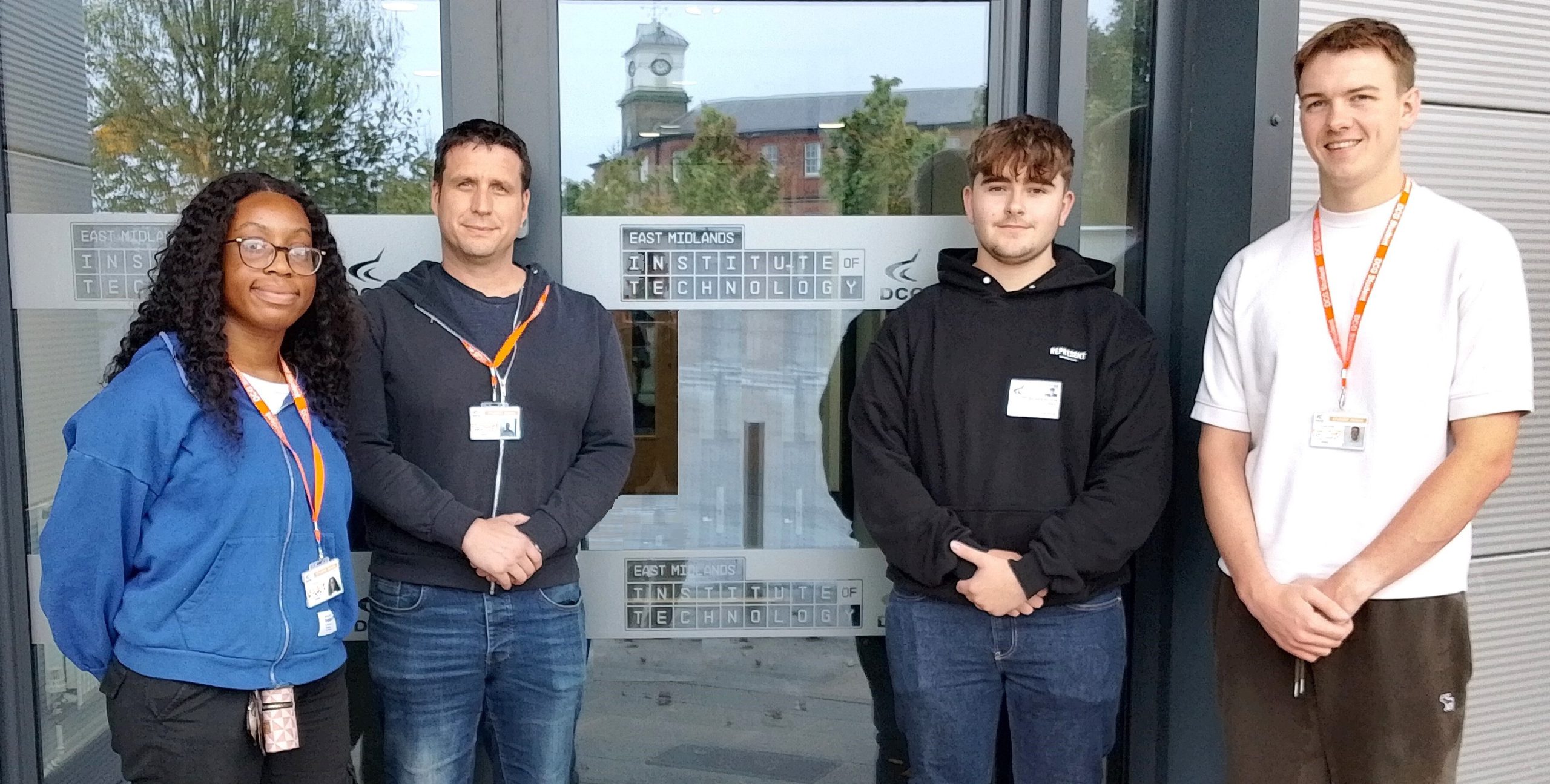 Four young people of various genders stood in front of a glass door.