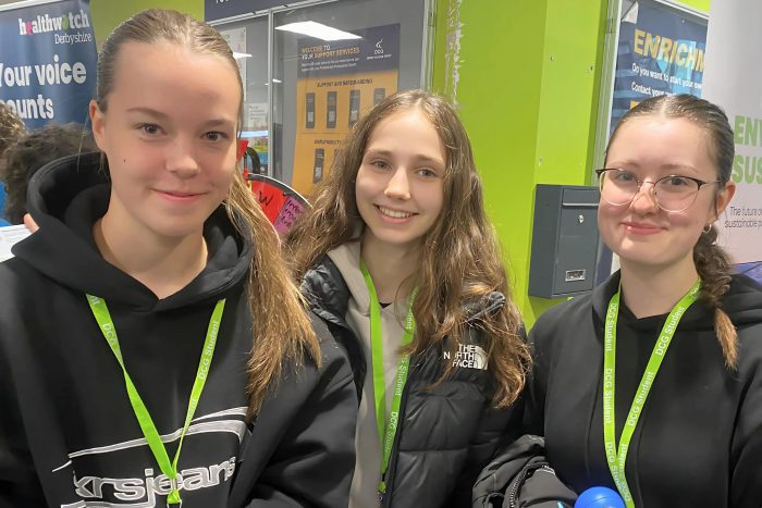 Three smiling young ladies wearing green lanyards.