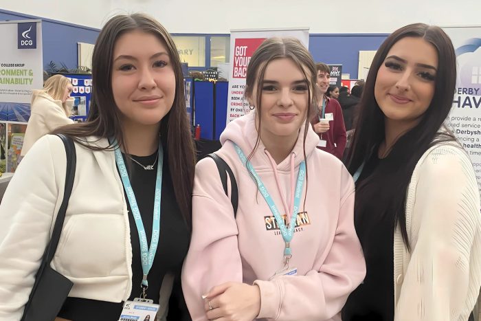 Three smiling young ladies at the Derby College Group Freshers' Fair wearing blue lanyards.