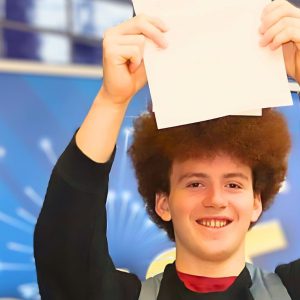 Young man with curly hair holding a peice of paper aloft.