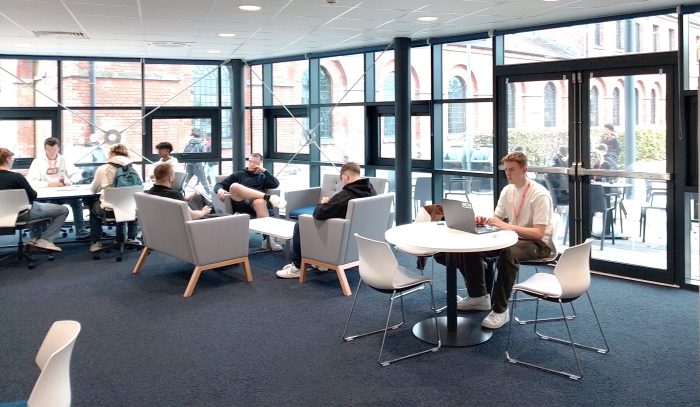 Young students sat at white tables in Derby College's Institute of Technology using laptops.