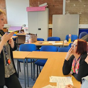 Woman stood signing to two other ladies sat at a table