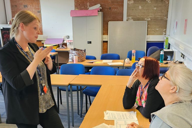 Woman stood signing to two other ladies sat at a table