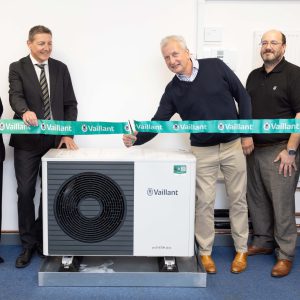 Four people stood by a fan with one man cutting a ribbon.