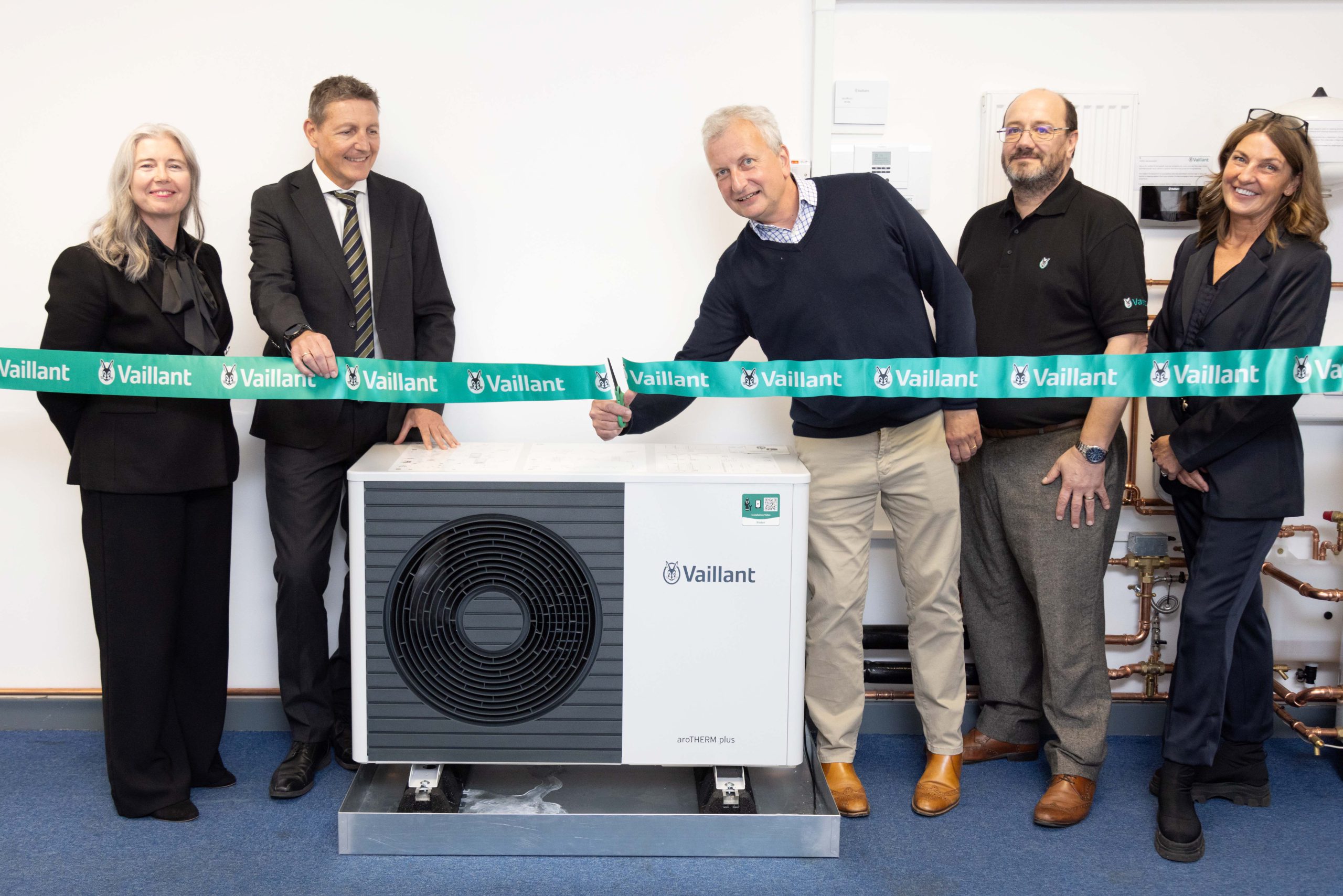 Four people stood by a fan with one man cutting a ribbon.