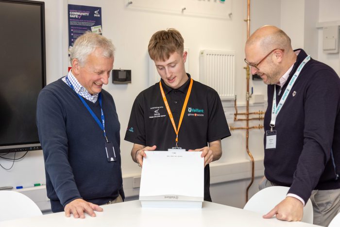 A young male Derby College student showing two men a boiler.