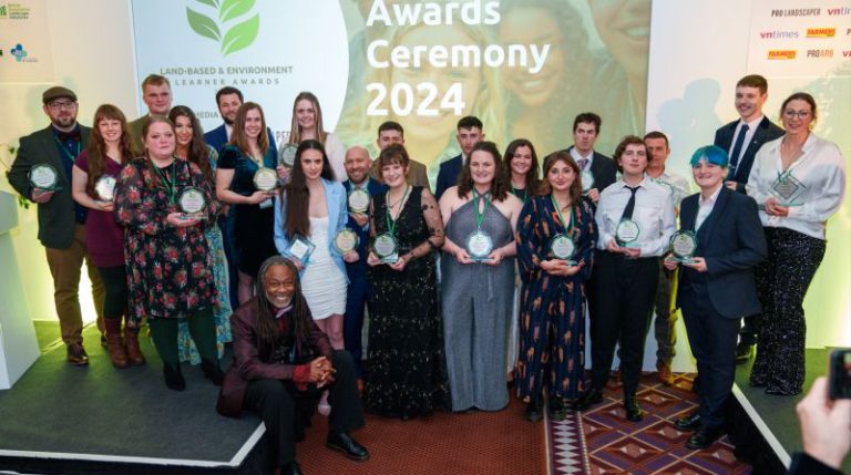 A group of people of mixed genders and ages holding awards at an awards ceremony.