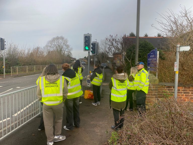 A group of young students wearing hi-viz jackets stood by a traffic light.