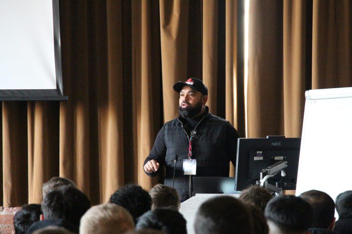 Man with a beard delivering a presentation to a group of students.