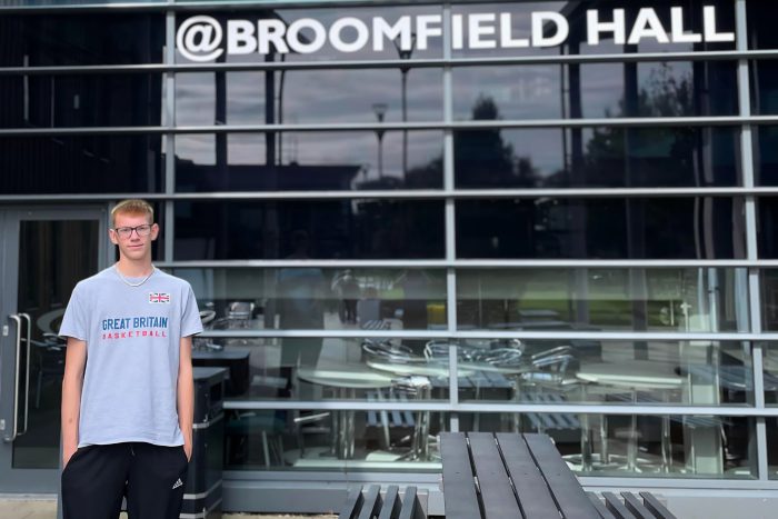 Student wearing a blue t-shirt and tracksuit bottoms stood outside of Haddon Building at Broomfield Hall.