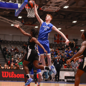 Two people playing basketball, one is scoring a slam dunk.