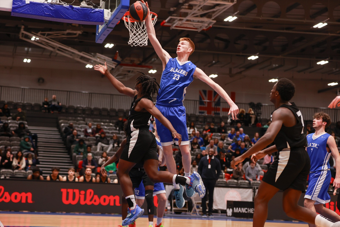 Two people playing basketball, one is scoring a slam dunk.