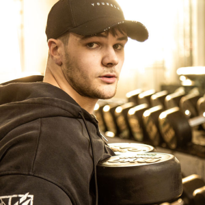 Young man wearing a black hoodie and baseball cap lifting dumbells