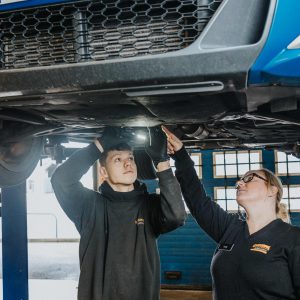 Young lady showing a young man how to work on the underside of a car.