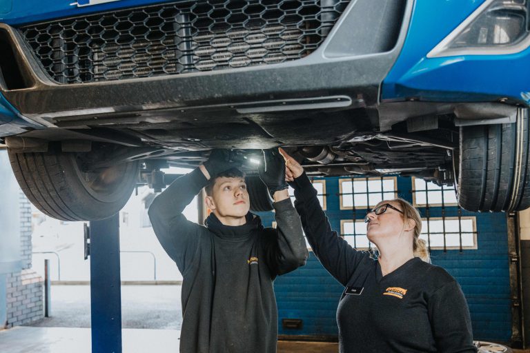 Young lady showing a young man how to work on the underside of a car.