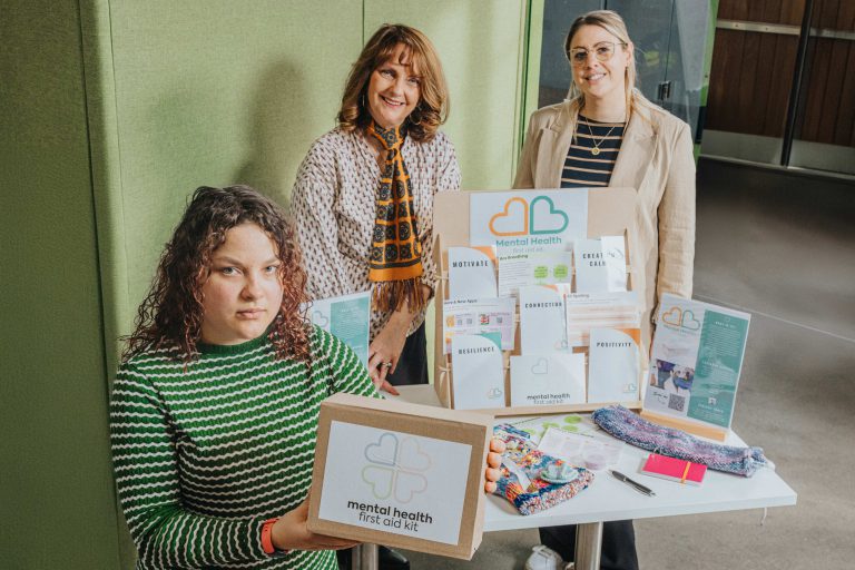 Three ladies holding pieces of a mental health toolkit.