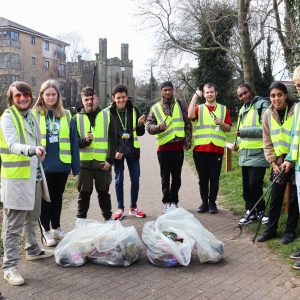 A group of students wearing Hi-Viz vests holding litter pickers, stood in front of full bin bags.