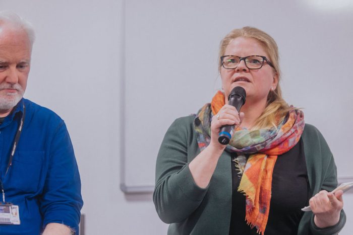 Person wearing a green cardigan and black shirt, speaking into a microphone