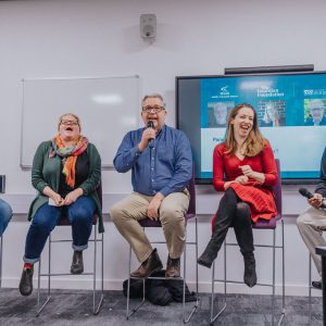 Five speakers sat on stools in front of a screen holding microphones.