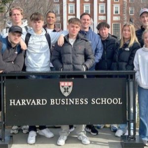 Young people stood in a group around a sign that reads 'Harvard Business School'.