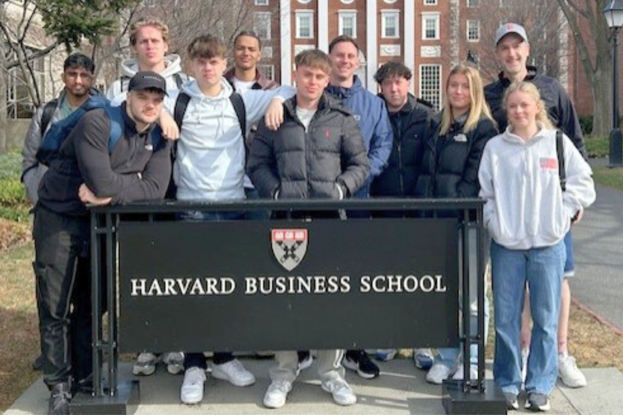 Young people stood in a group around a sign that reads 'Harvard Business School'.